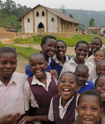 Een kerkgebouw in Uganda met een groep lachende kinderen op de voorgrond.