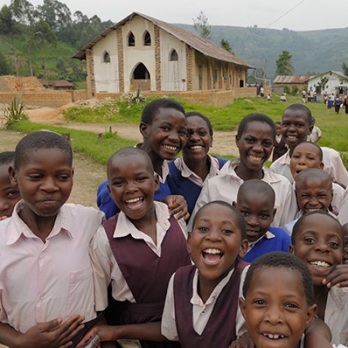 Een kerkgebouw in Uganda met een groep lachende kinderen op de voorgrond.