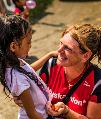 Vrouw met shirt van de Muskathlon aan lacht naar meisje.