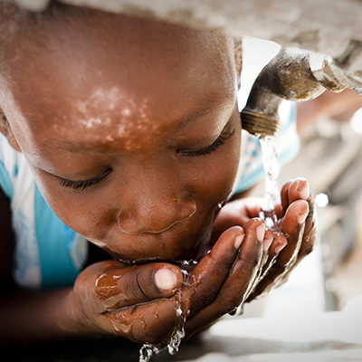 Een jongen uit Haïti drinkt water uit een kraan.