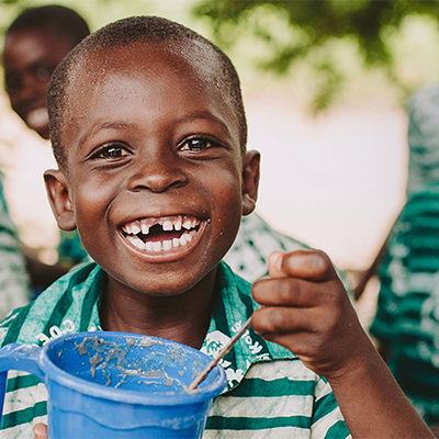 Een lachend kind eet uit een blauwe mok.