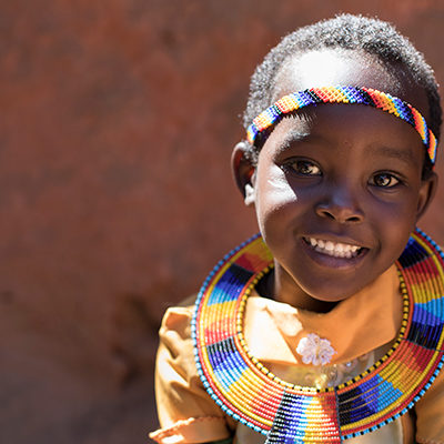 Afrikaans meisje in traditionele kleding lacht in de camera.