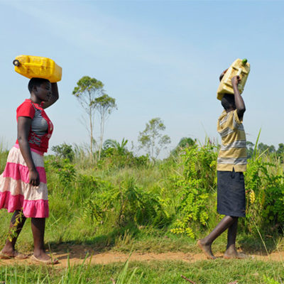 Twee afrikaanse tieners lopen met jerrycans op hun hoofd.