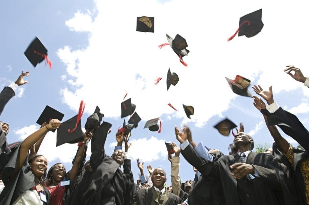 Jongeren in graduation-jurk gooien hun hoedjes in de lucht