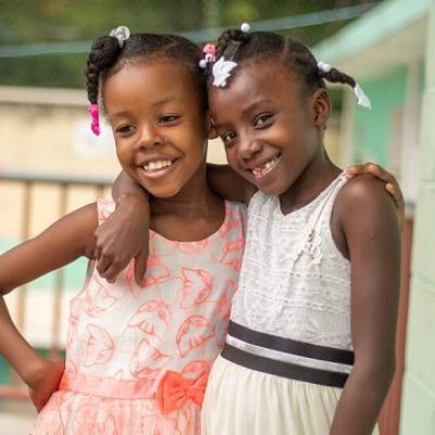 Twee meisjes uit Haïti staan gearmd op een balkon.