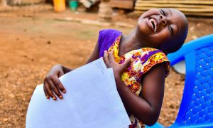 Een meisje houdt een brief van haar sponsor vast en lacht vrolijk.