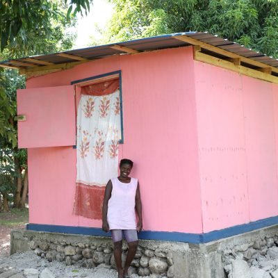 Een vrouw staat bij haar heropgebouwde huis na de aardbeving in Haïti.