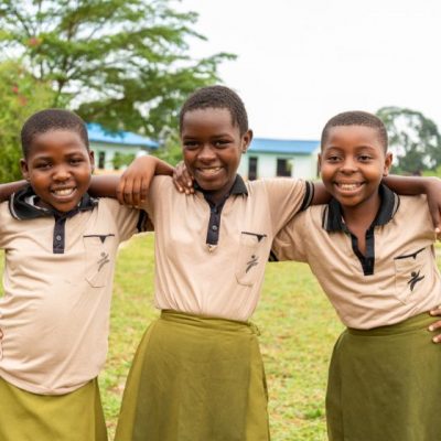 Drie meisjes staan arm in arm op een rij in hun schooluniform.