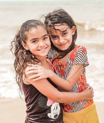 Twee meisjes staan op het strand en omhelzen elkaar.
