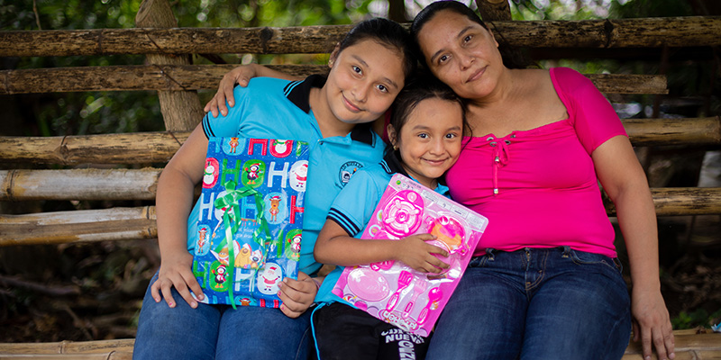 Karla uit El Salvador zit met haar moeder en zusje op een bankje met hun kerstcadeaus. 