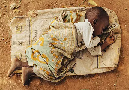 Een jongetje ligt te slapen op een zak op de grond.