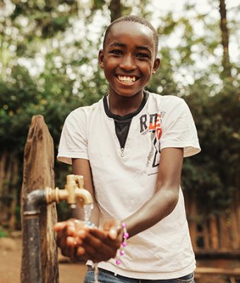 Een Keniaanse jongen lacht en laat water over zijn handen lopen.