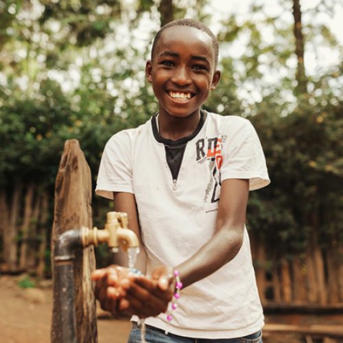 Een Keniaanse jongen lacht en laat water over zijn handen lopen.