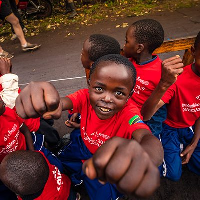 Een jongen uit Tanzania met een shirt van de Muskathlon aan, kijkt in de camera.
