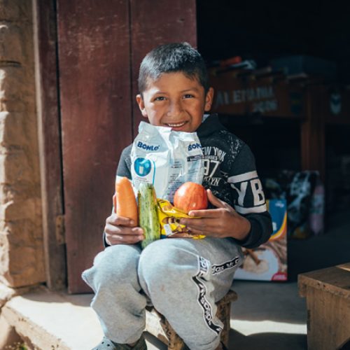 Een jongen houdt een voedselpakket vast en zit op de drempel van zijn huis.