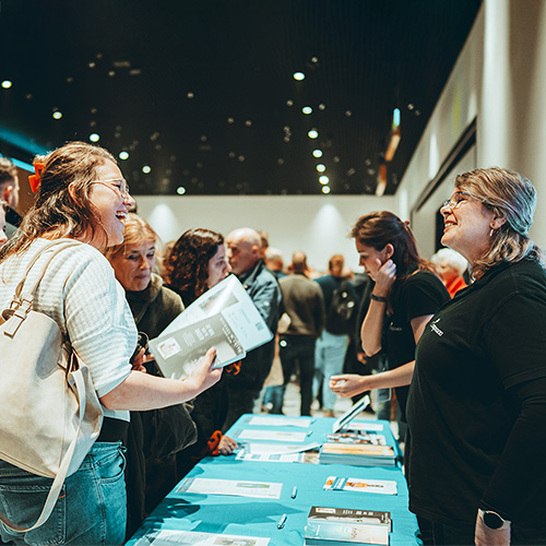 Een eventambassadeur is bij de Compassion-stand in gesprek met een bezoeker van het concert