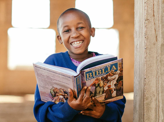 Een jongen uit Tanzania houdt een opengeslagen kinderbijbel vast.