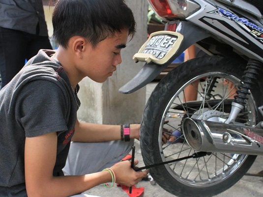 Indonesische jongen sleutelt aan een motor.