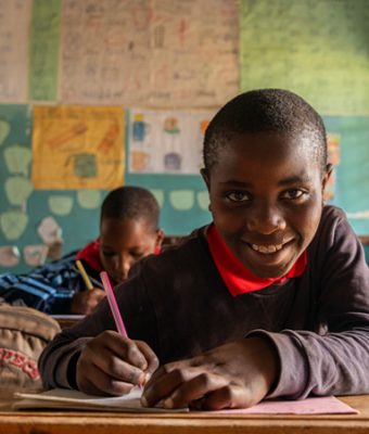 Pascal uit Tanzania zit in een schoolbank en schrijft in een werkboek.