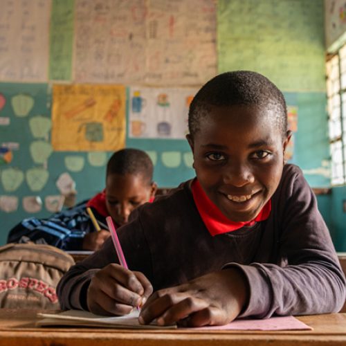 Pascal uit Tanzania zit in een schoolbank en schrijft in een werkboek.