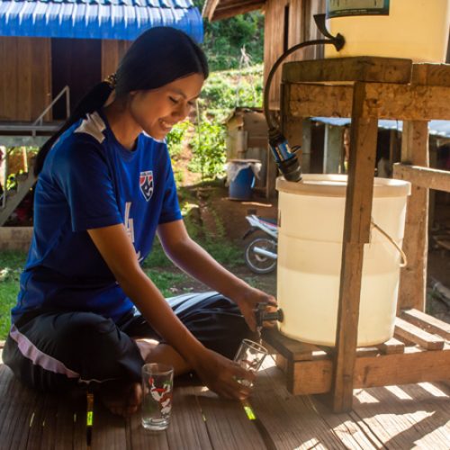 Vimala uit Thailand tapt water uit de nieuwe waterfilter bij haar huis.