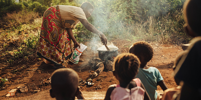 Een vrouw kookt buiten in Kenia met een groep kinderen om haar heen.