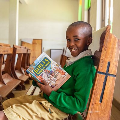 Een jongen zit in een kerkbank en houdt een kinderbijbel vast.