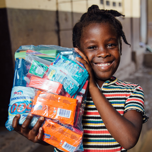 Een meisje uit Haïti laat blij een tas vol boodschappen zien.