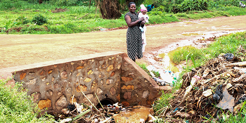 Gladys staat met haar dochter Miracle bij het riool in een van de sloppenwijken van Uganda.
