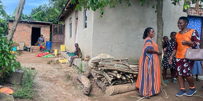 Moeder Teddy uit Uganda staat samen met projectmedewerker Kezia bij een stapel brandhout. 