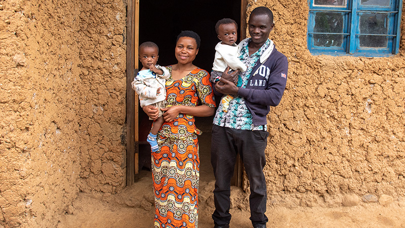 Jeannette uit Rwanda staat met haar man en tweeling voor hun huis