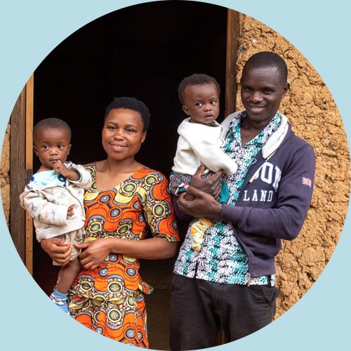 Jeannette uit Rwanda staat met haar man en tweeling voor hun huis.