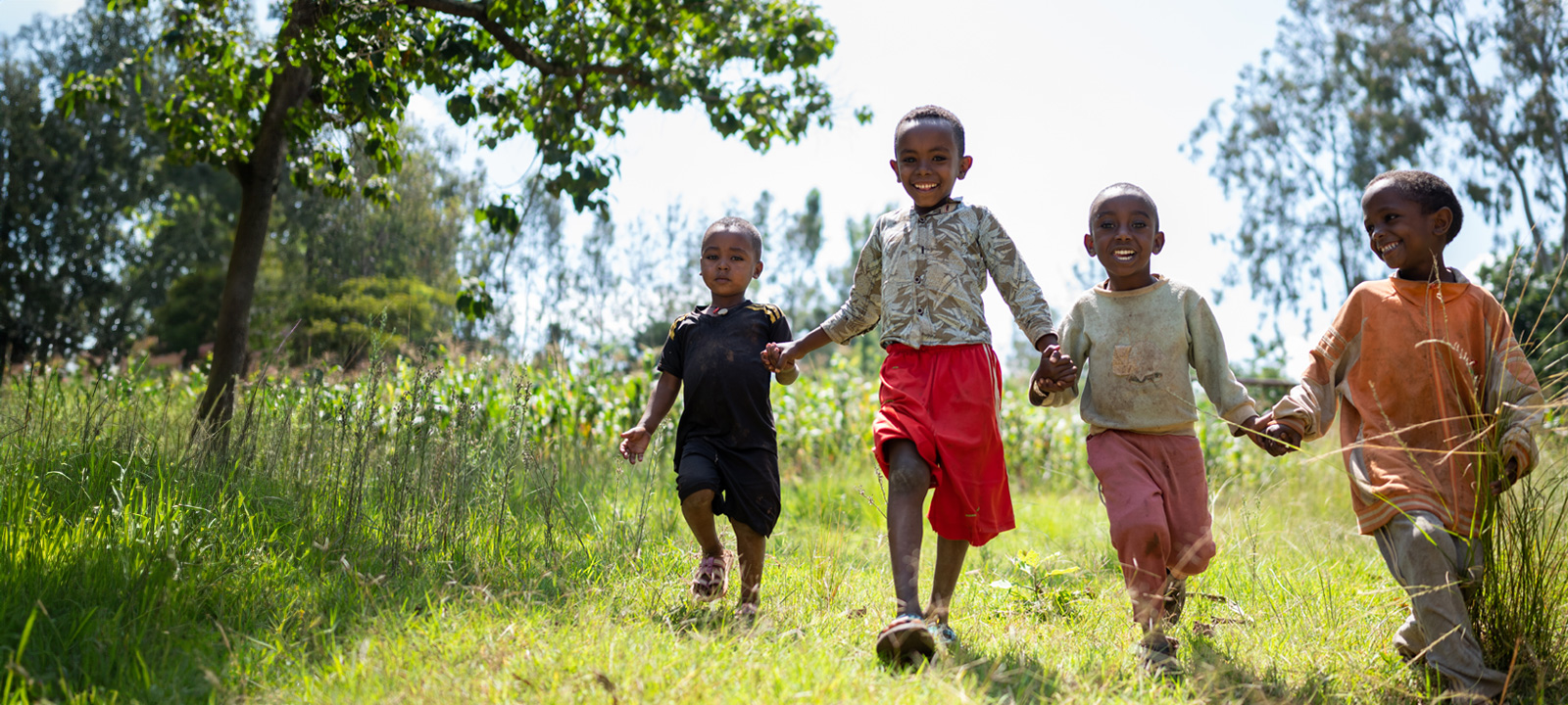 Vier Ethiopische kinderen rennen hand in hand door het gras.