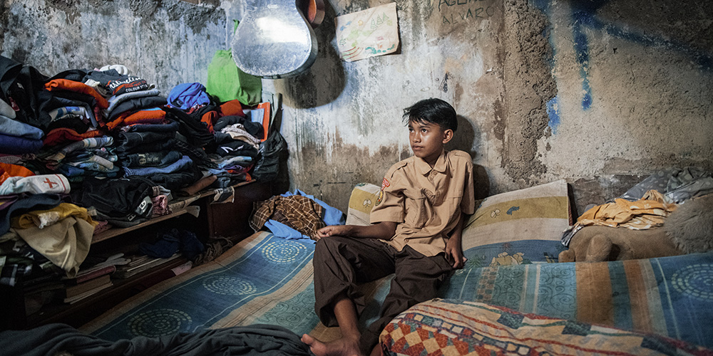Agung uit Indonesië zit in zijn slaapkamer.