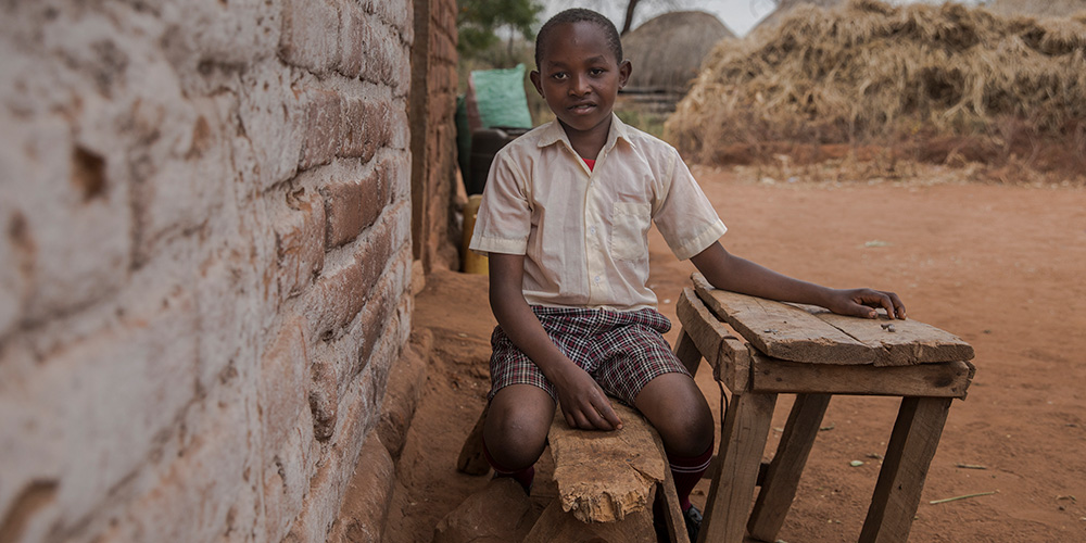 Dennis uit Kenia zit op een bankje voor zijn huis.