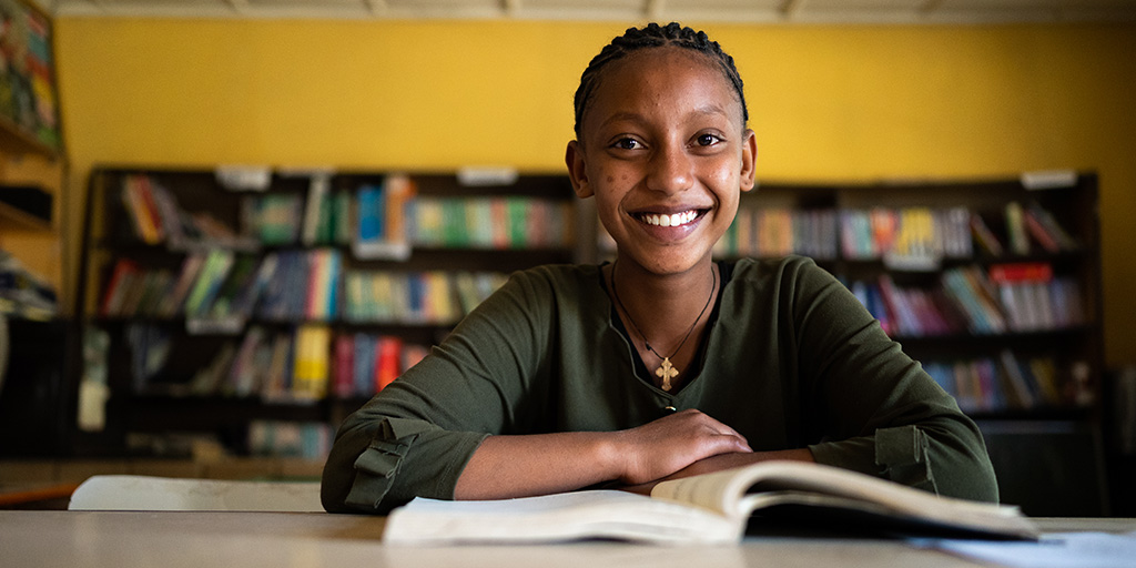 Tanzaniaans meisje zit met haar boek aan tafel.
