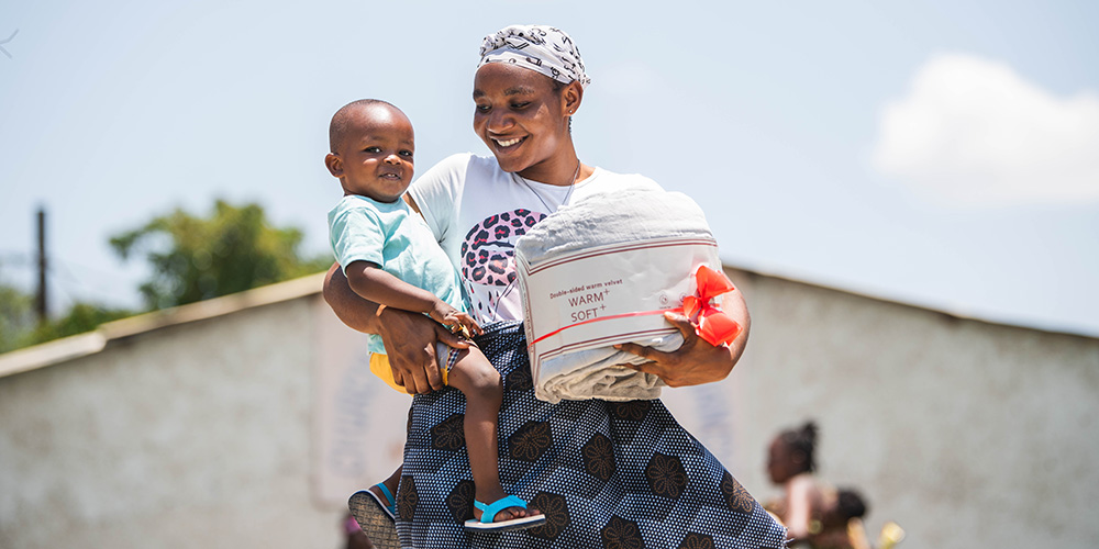 Gertrude uit Zambia draagt haar zoon Malakai op de arm, in de andere hand heeft ze een deken.