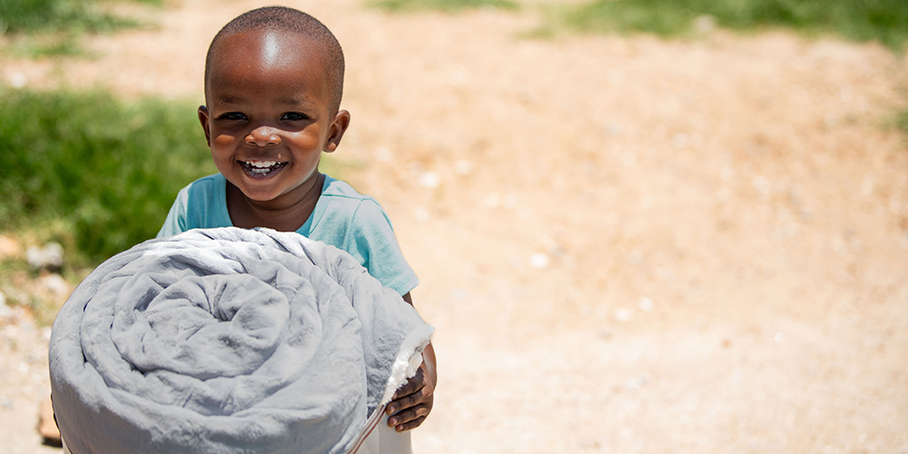 Malakai uit Zambia kijkt lachend in de camera met zijn gekregen deken.