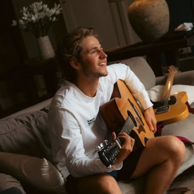 Marc Floor zit op een bank en speelt gitaar.