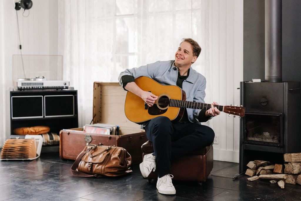 Matthijn Buwalda zit op een poef en speelt gitaar.