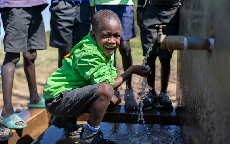 Leshan uit Kenia vangt met zijn handen water op dat uit een kraan stroomt.