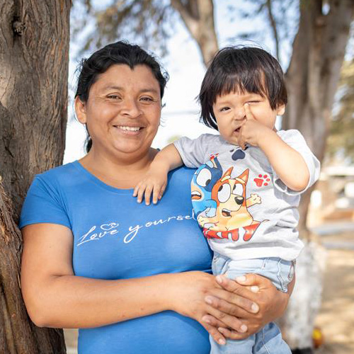 Maricarmen uit Peru staat met haar jongste zoon voor een boom.
