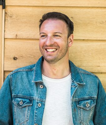 Artiest Daniël Marx staat voor een houten gebouw.