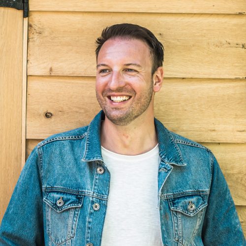 Artiest Daniël Marx staat voor een houten gebouw.