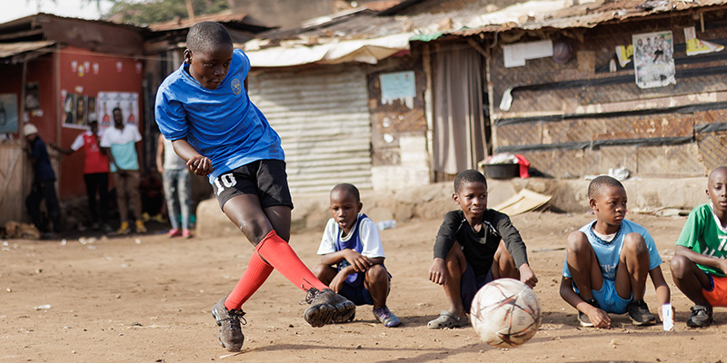 Jordan uit Uganda neemt een penalty terwijl zijn vrienden toekijken.
