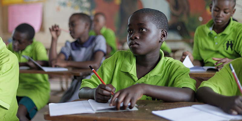 Jordan zit met een potlood in zijn hand in de schoolbanken op een Compassion-project in Uganda.