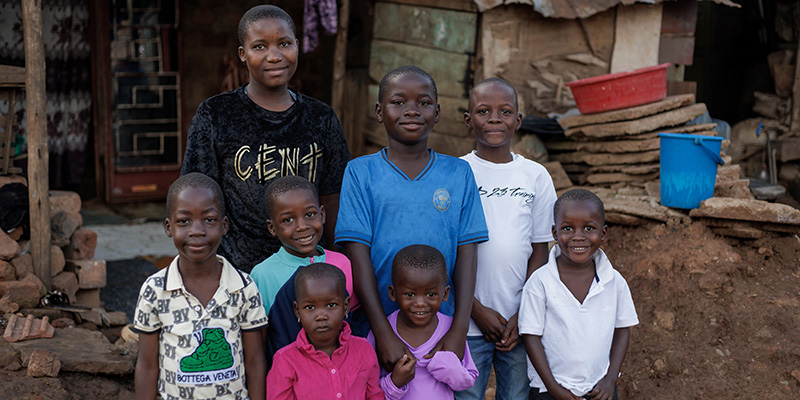 Jordan uit Uganda staat samen met zijn neefjes en nichtjes voor hun huis.