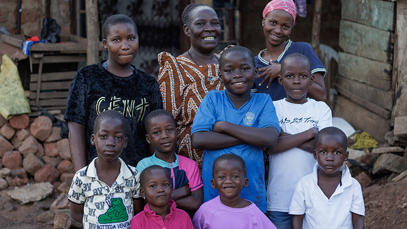 Oma Prossy met haar klein- en achterkleinkinderen voor haar huis in Uganda.
