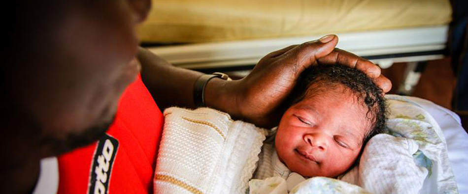 Een Ugandese vader houdt zijn pasgeboren dochter vast.