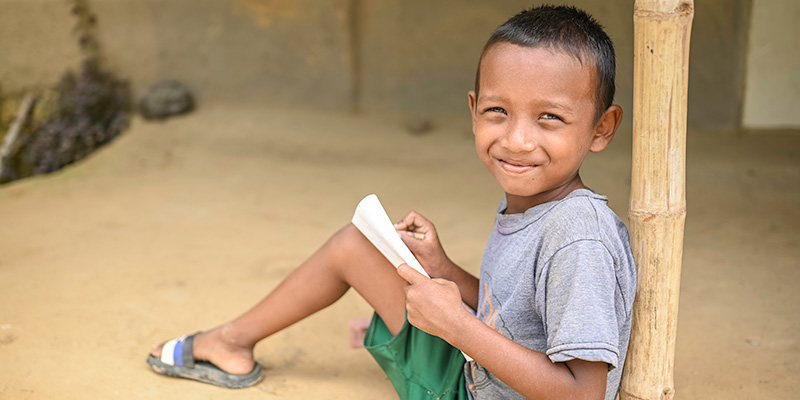 Johan uit Bangladesh zit tegen een paal aan met papieren in zijn hand. 